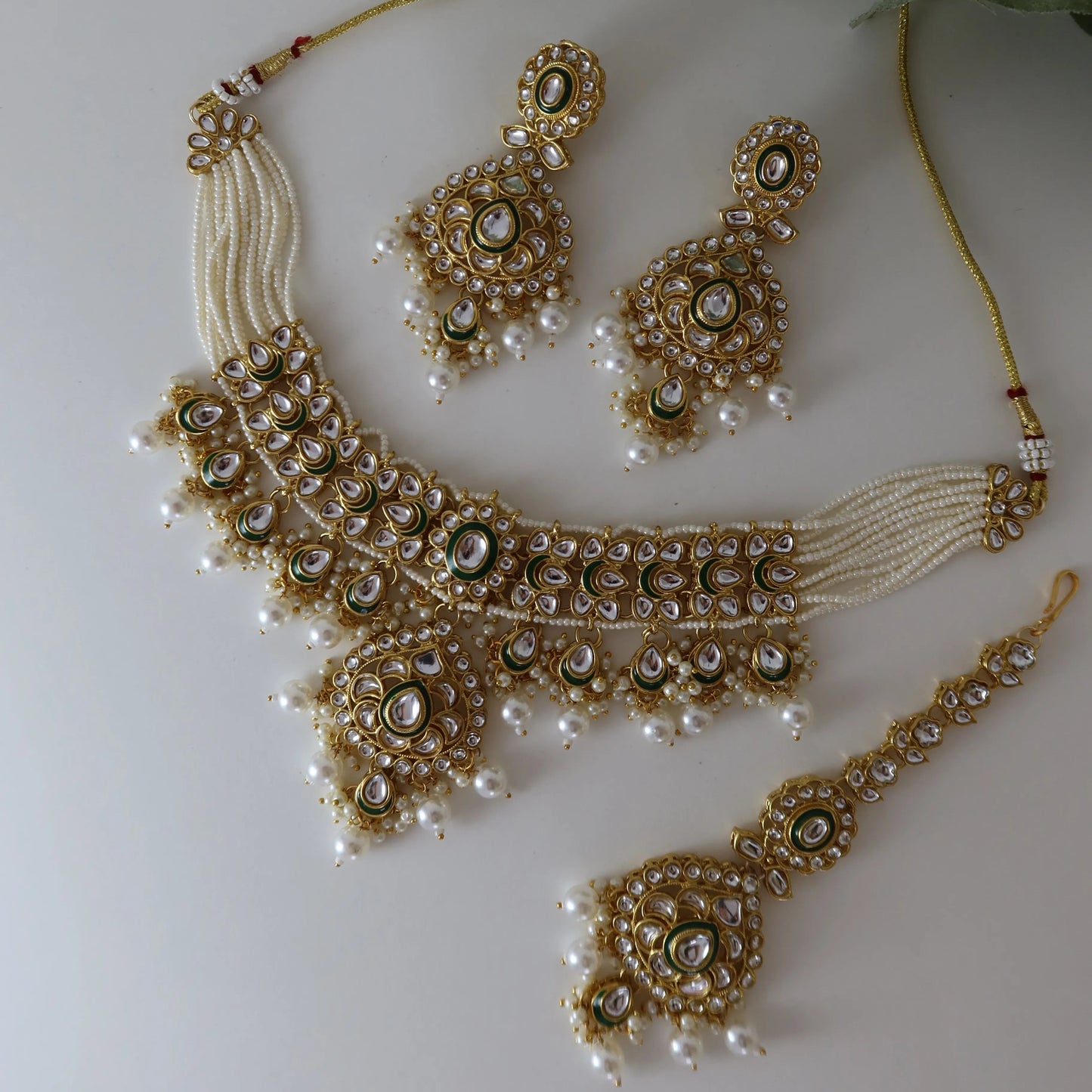 Jewelry set with necklace, earrings, and haram on a white background with green leaves.