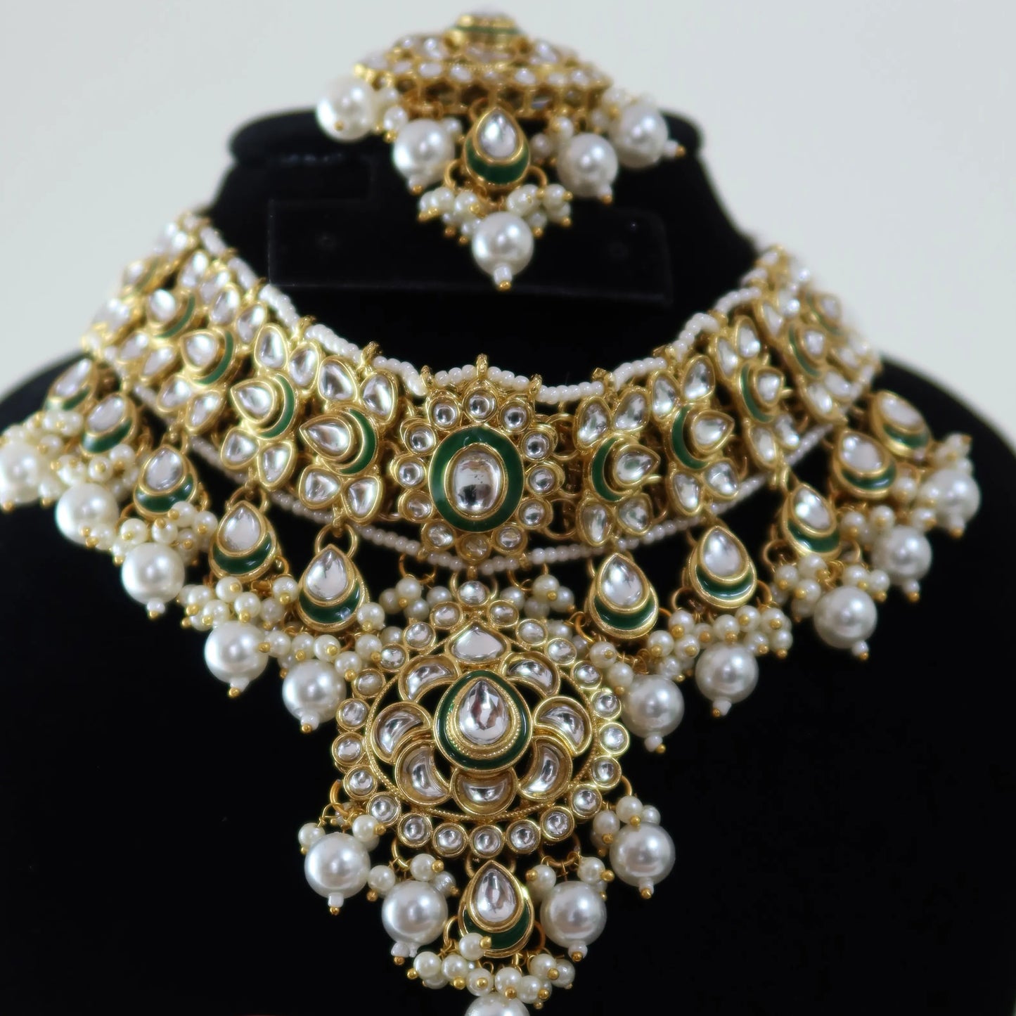 Ornate gold and pearl necklace on a mannequin bust with matching earrings held by a hand.