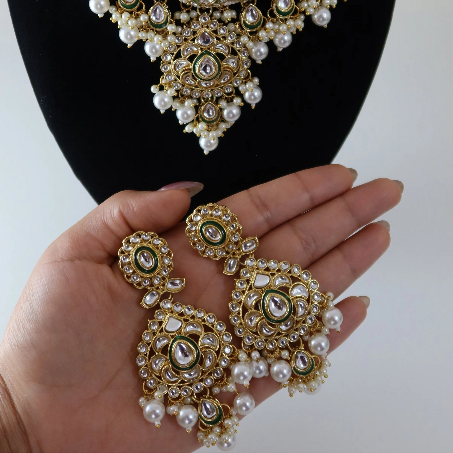 Gold and pearl jewelry set on a mannequin and held in a hand against a white background