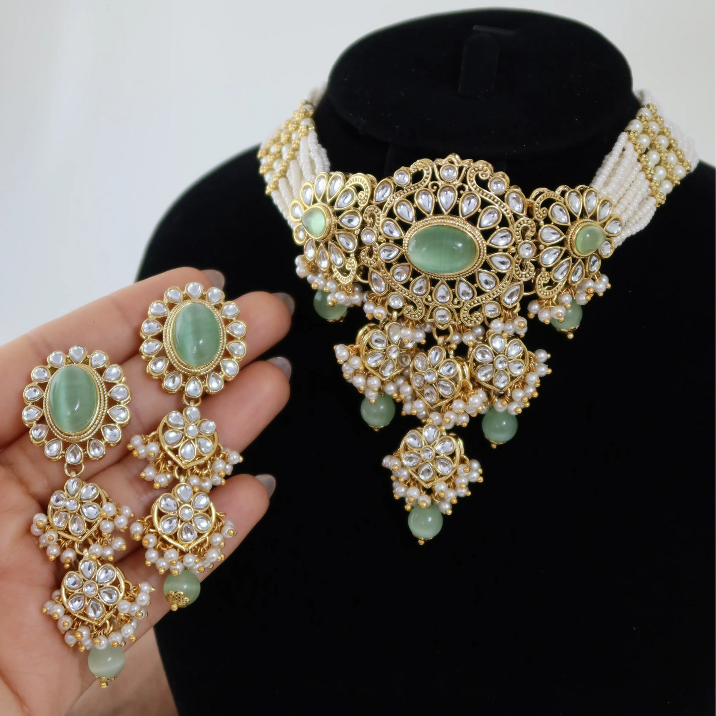 Gold necklace with green gemstones on a black stand, held by a hand.