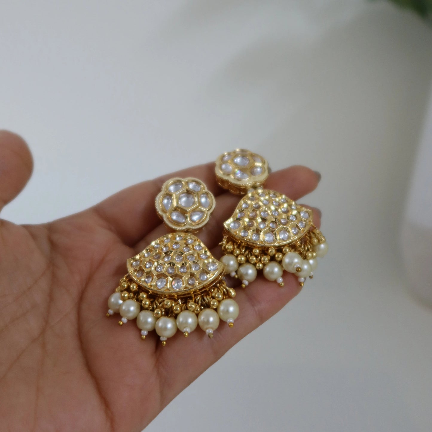 Gold and pearl earrings held in a hand with a blurred background