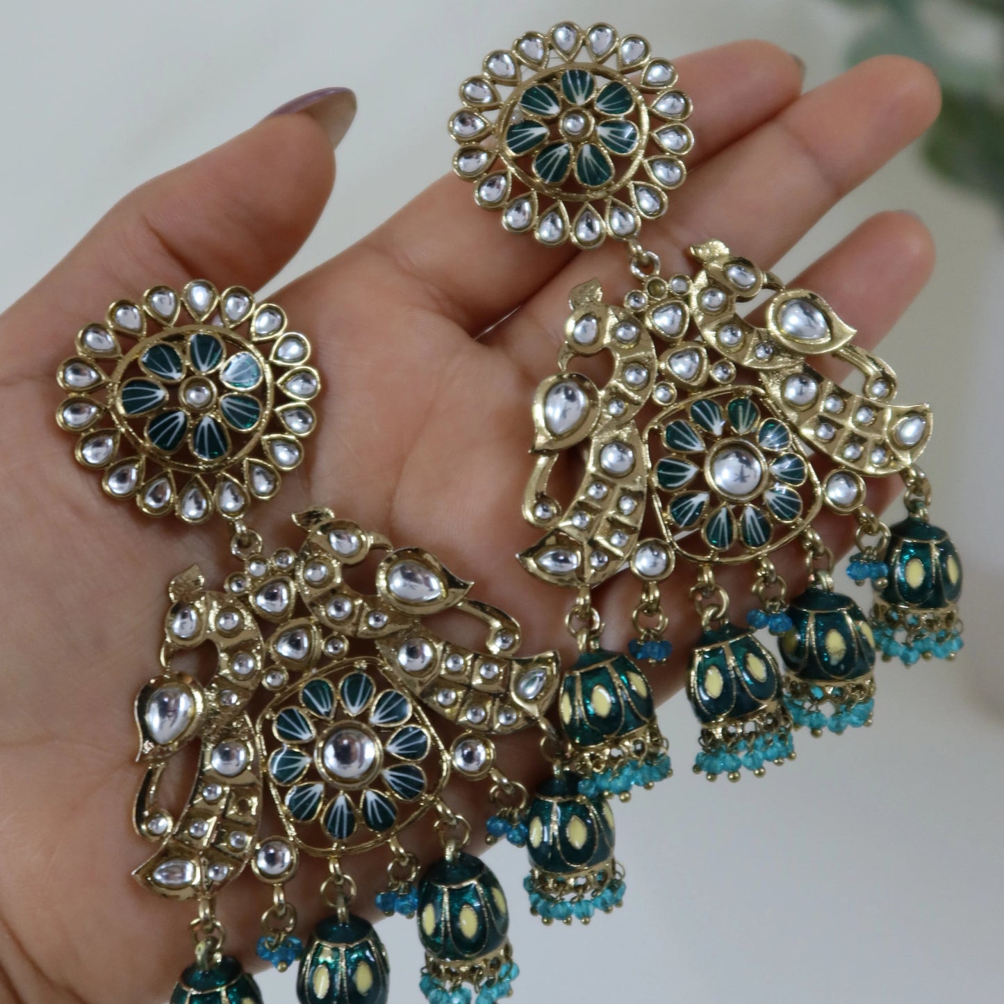 Ornate earrings with blue and gold details held in a hand against a neutral background