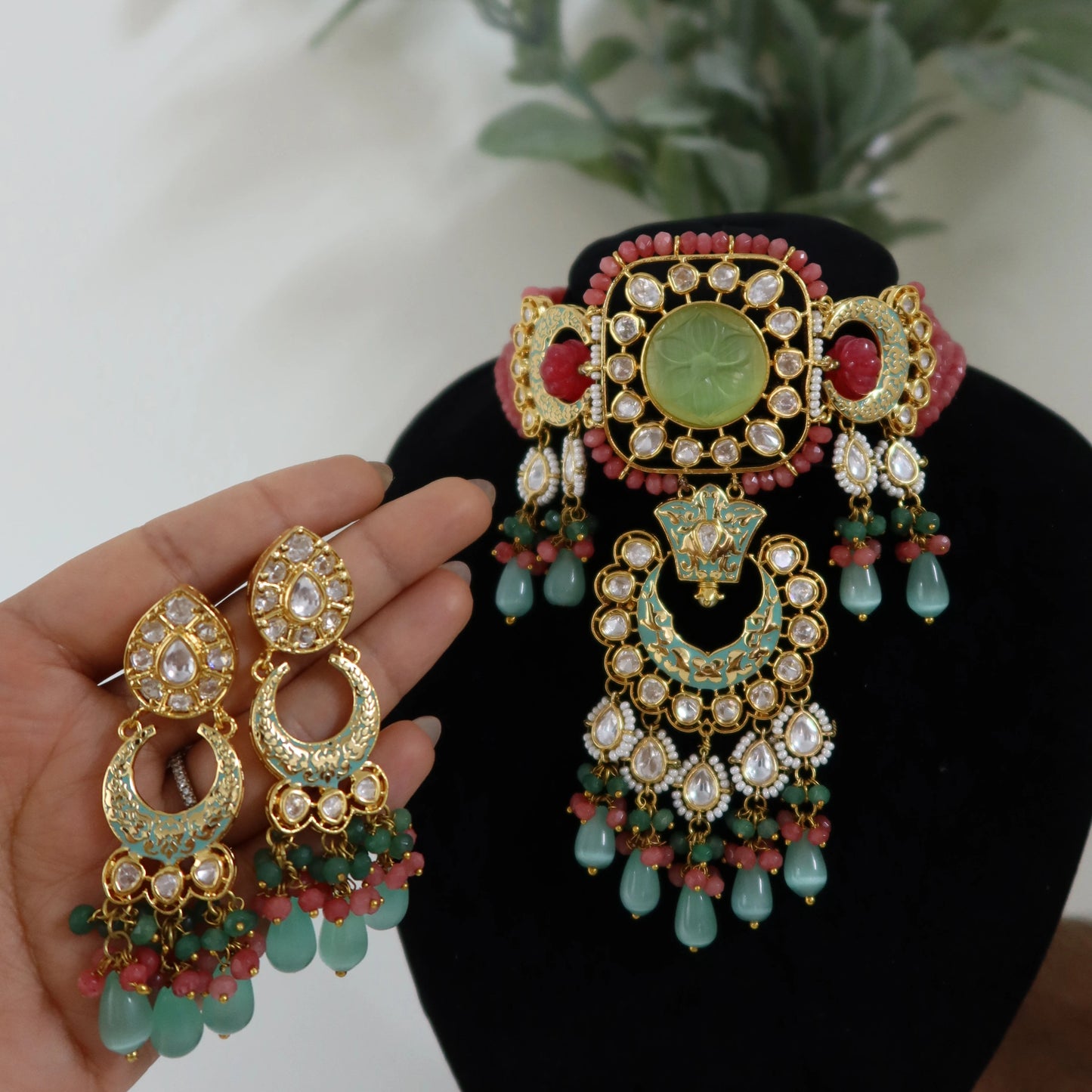 Ornate earrings with gold, green, and red details on a black stand.