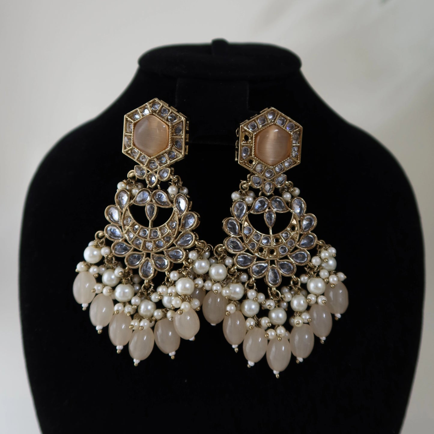 Pair of ornate earrings with pearls on a black stand against a white background