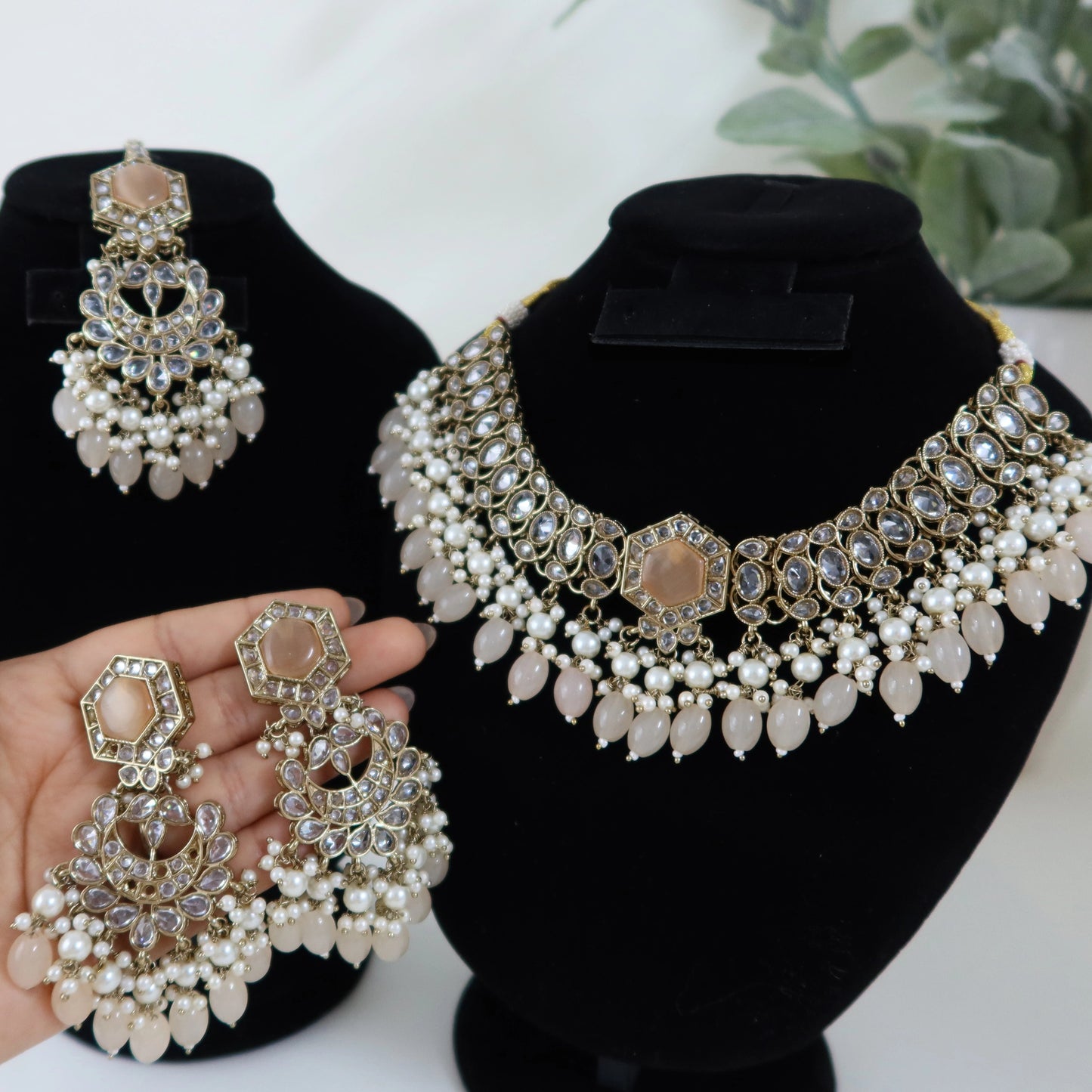 Pearl and gold jewelry set on black mannequin heads with a hand holding earrings.