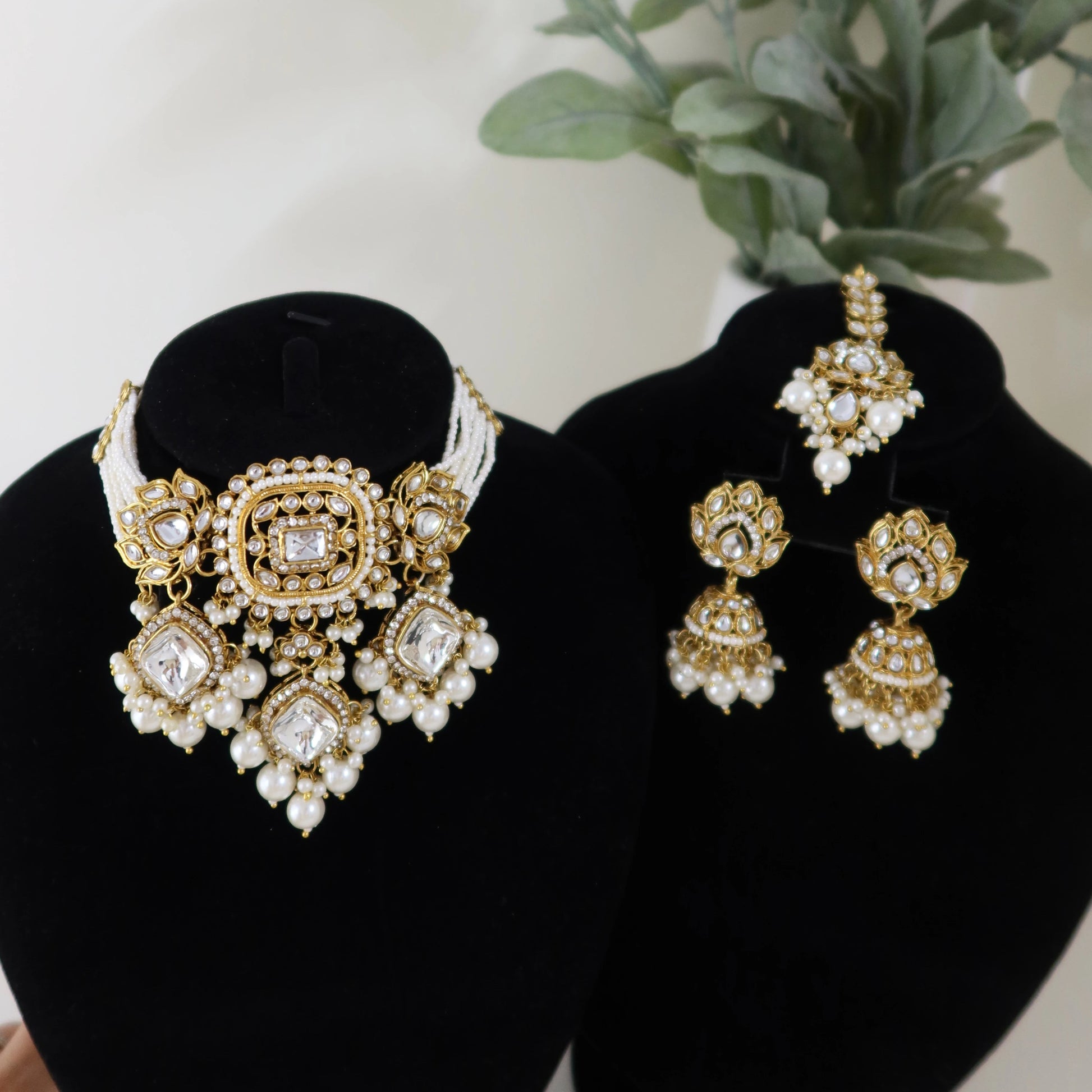 Gold and pearl jewelry set on black stands with a plant in the background