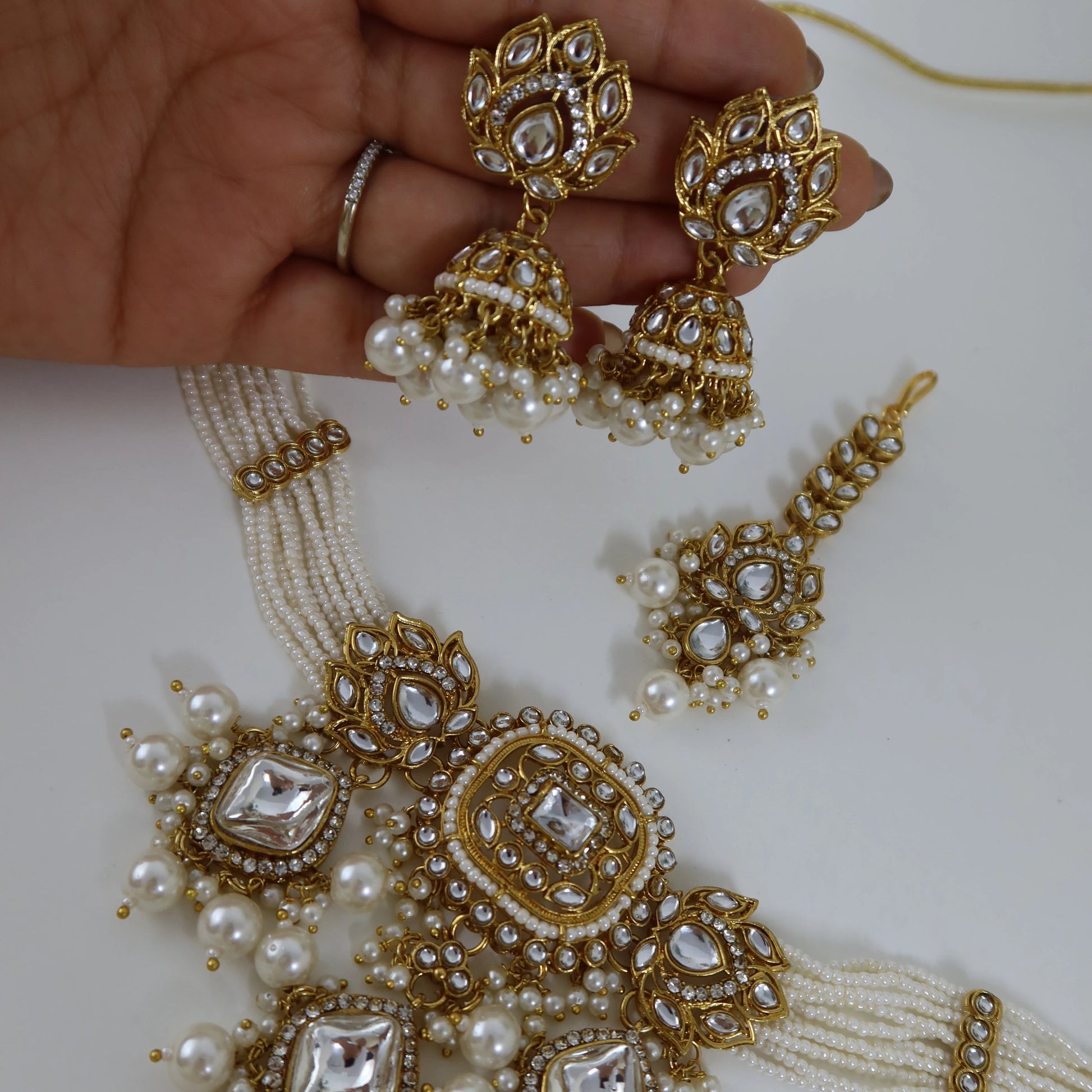 Gold and pearl jewelry set including earrings and a necklace on a white background.