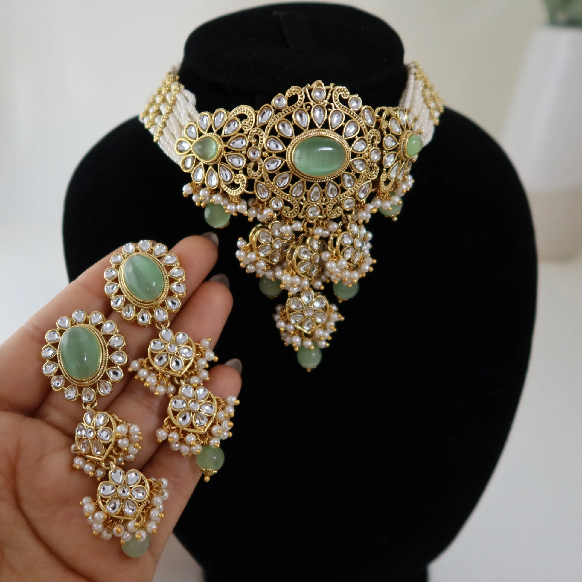 Gold and green gemstone jewelry set on a black stand with a hand holding earrings.