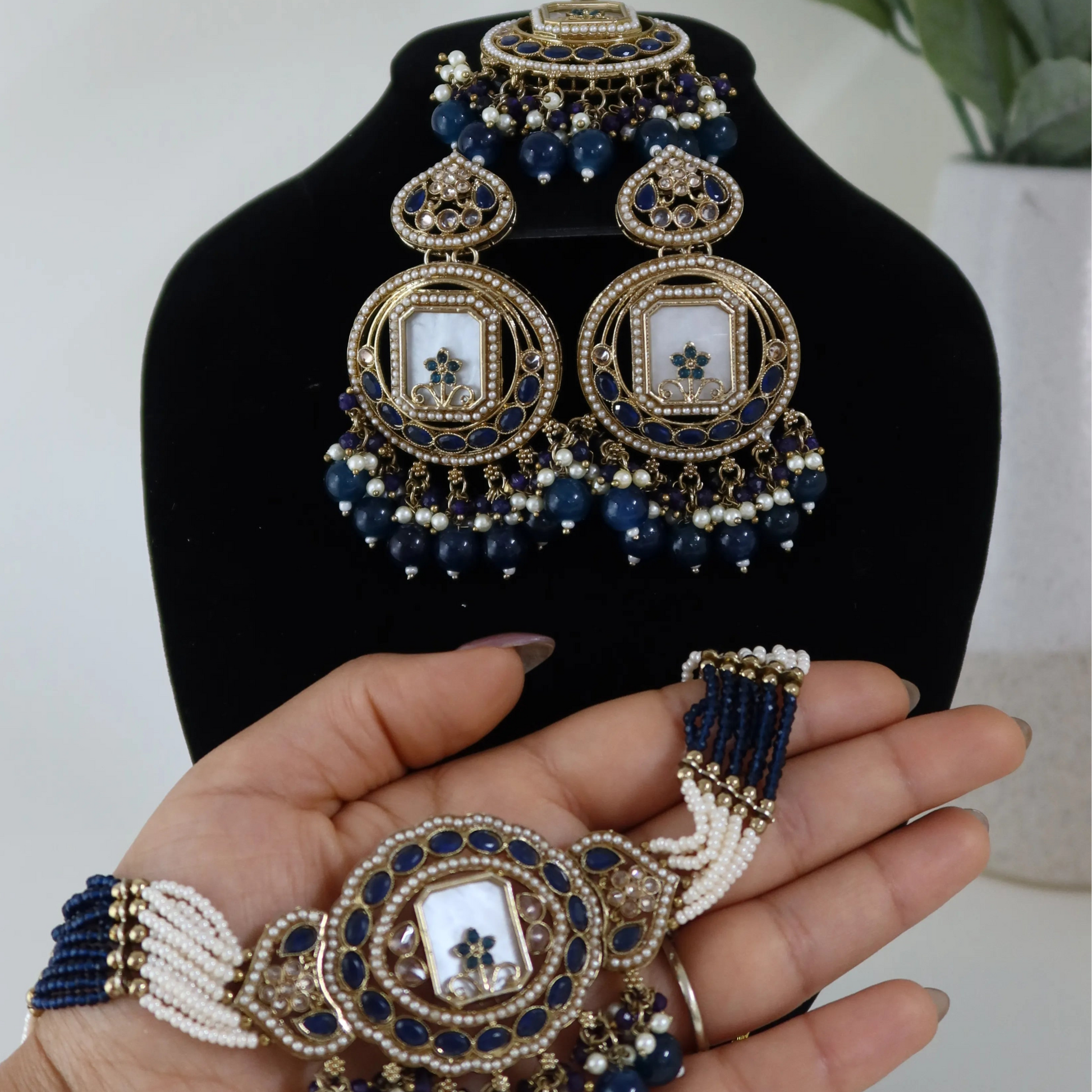 Jewelry set including earrings, necklace, and bracelet on a black stand with a hand holding a bracelet.