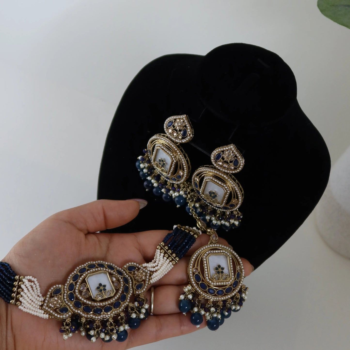 Decorative earrings held in a hand with a black velvet box in the background