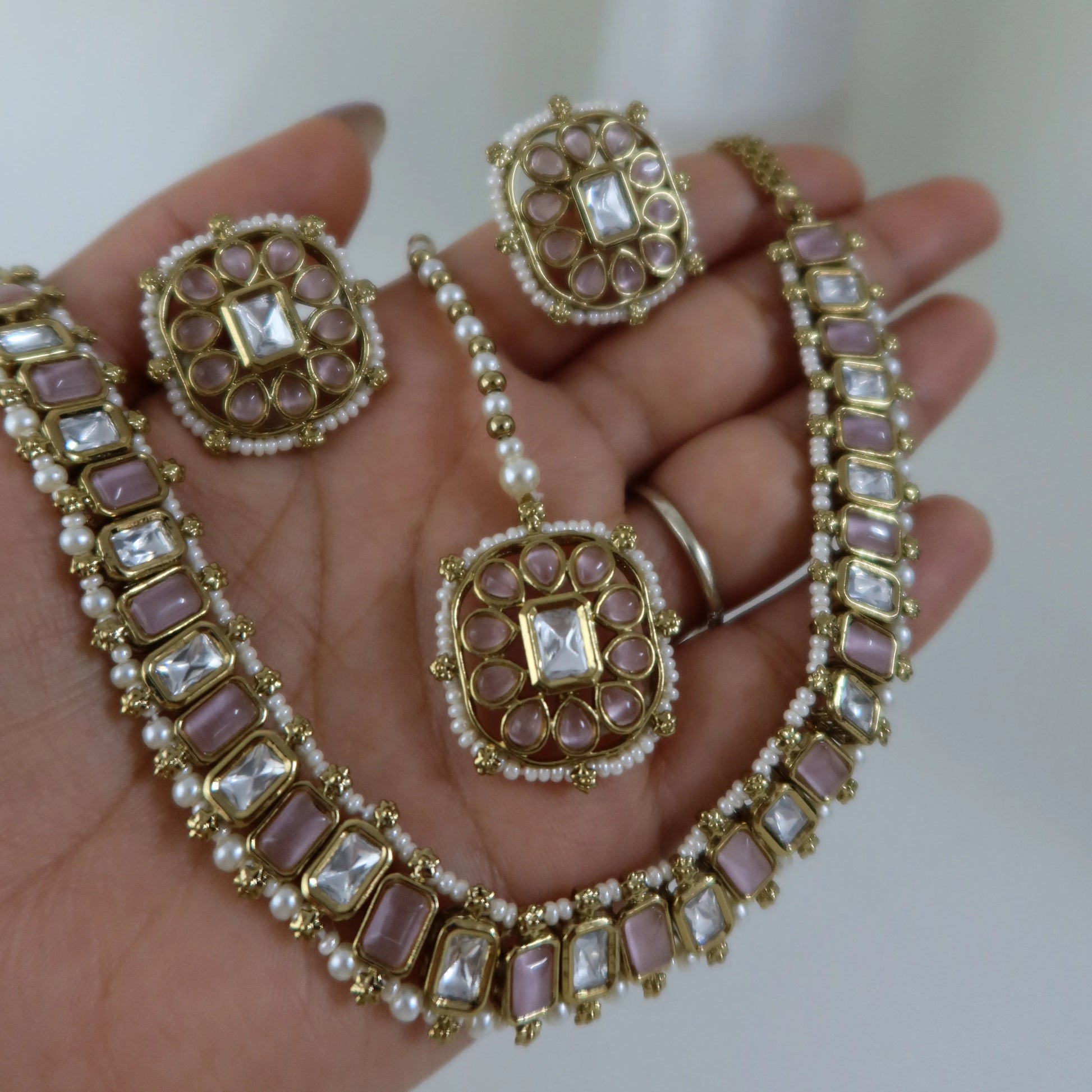 Gold and pearl jewelry set on a hand with a blurred background