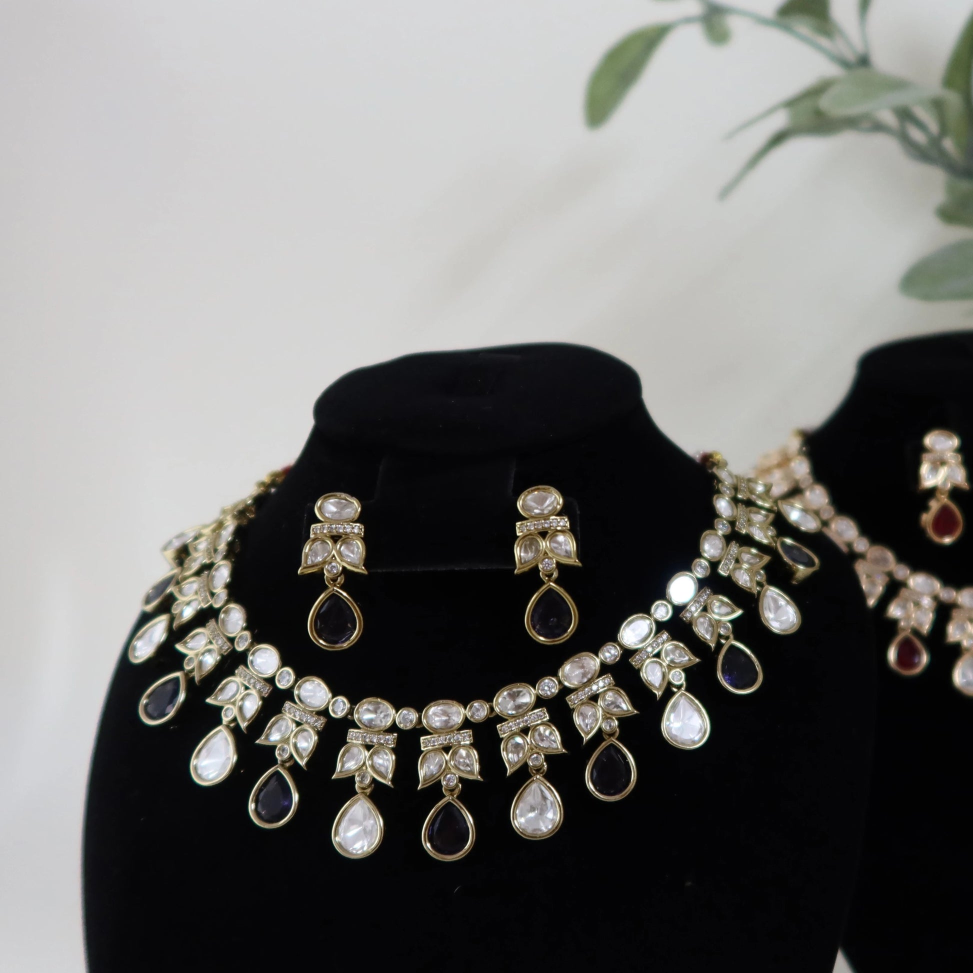 Jewelry set on black mannequin busts with a plant in the background