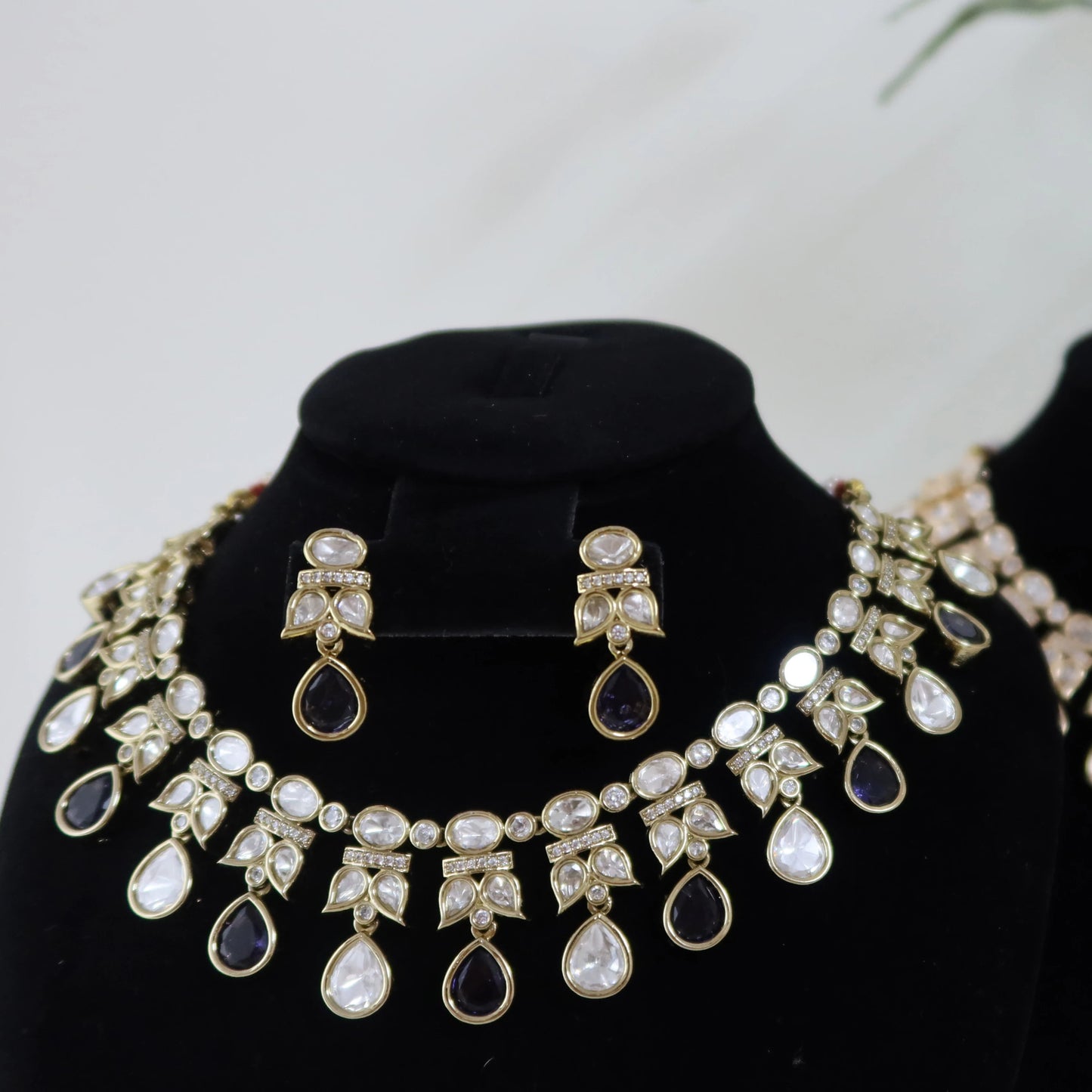 Two sets of jewelry on black mannequin heads with a blurred plant in the background.