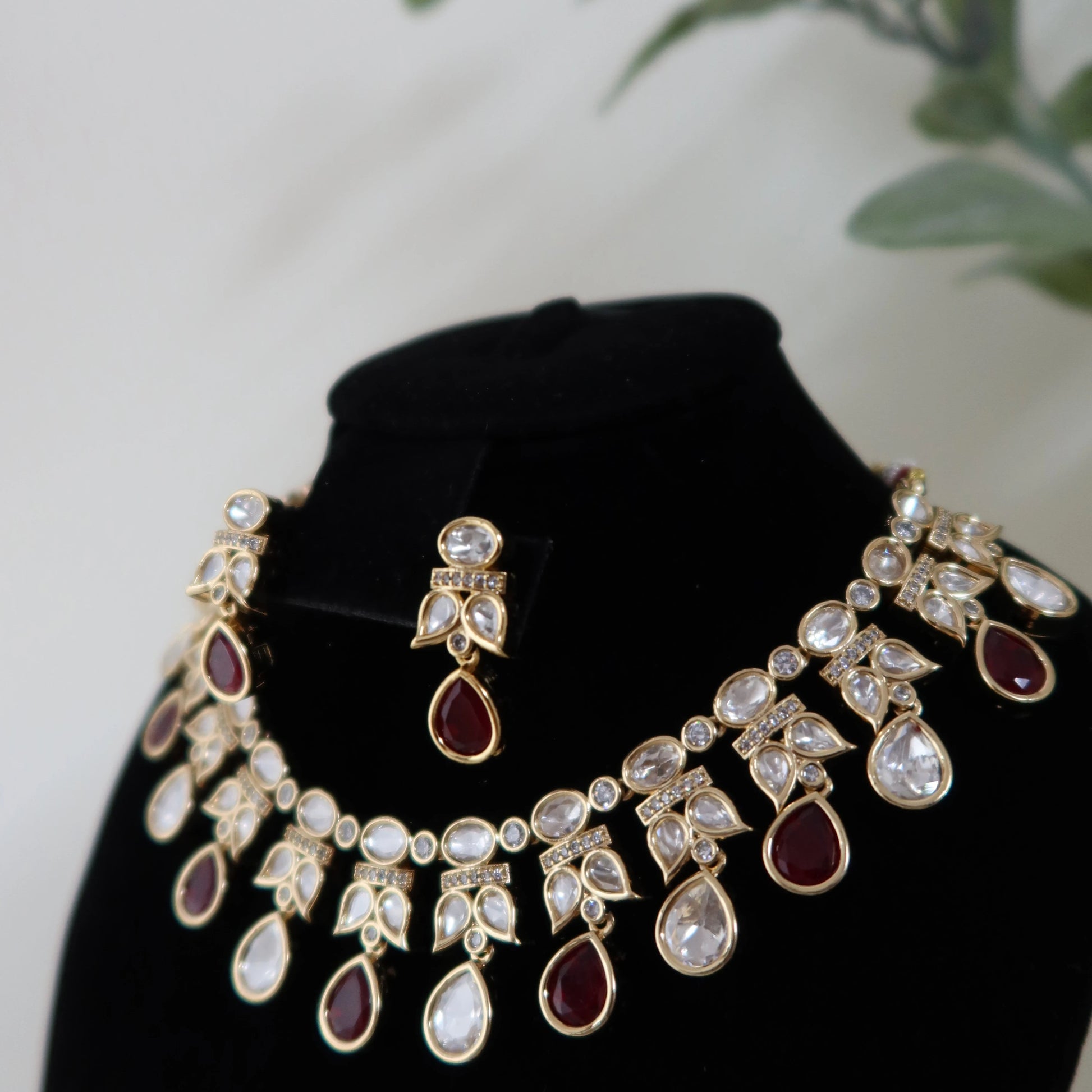 Jewelry set with necklace and earrings on a black stand with a blurred green plant background