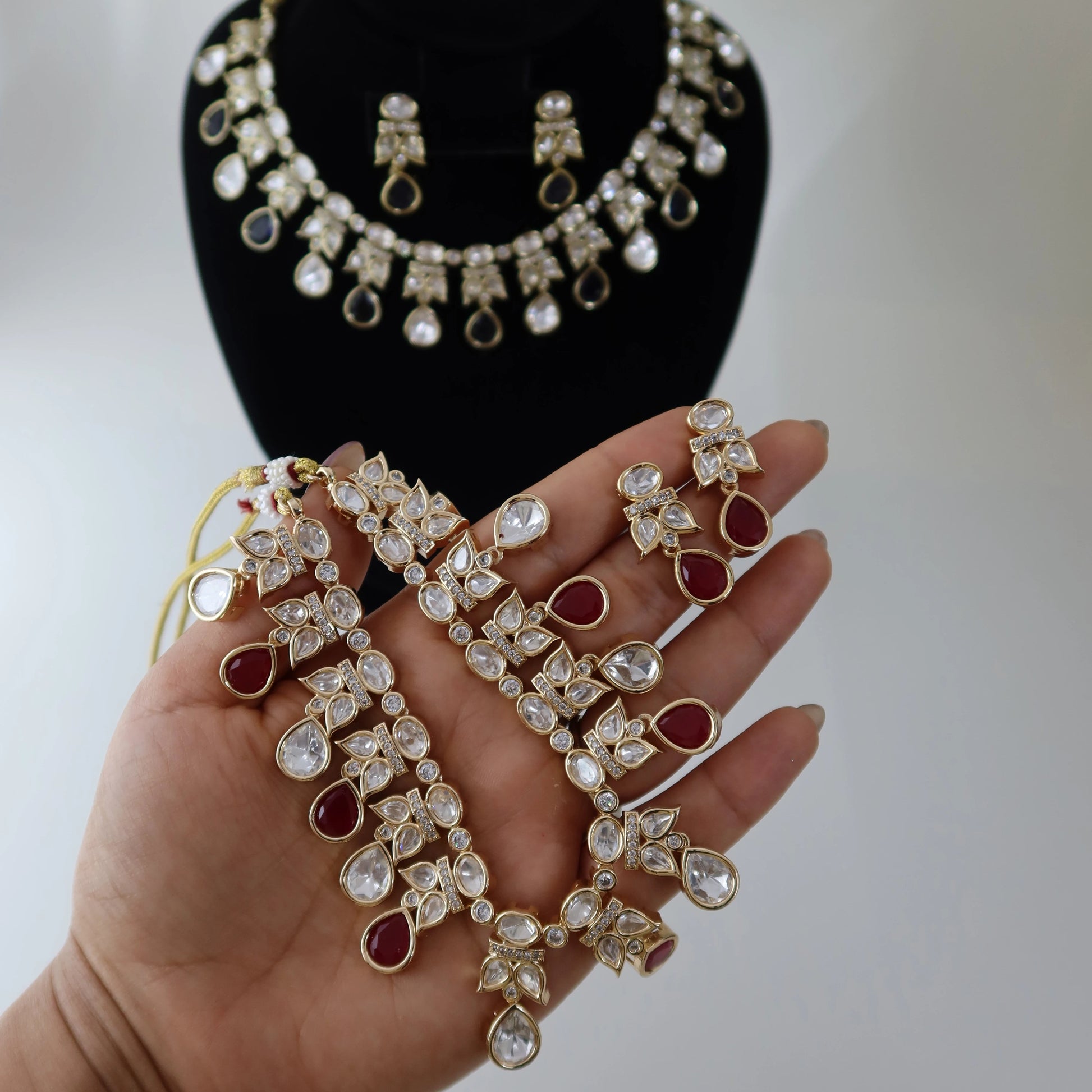Jewelry set including necklace, earrings, and bangles on a mannequin and held by a hand.