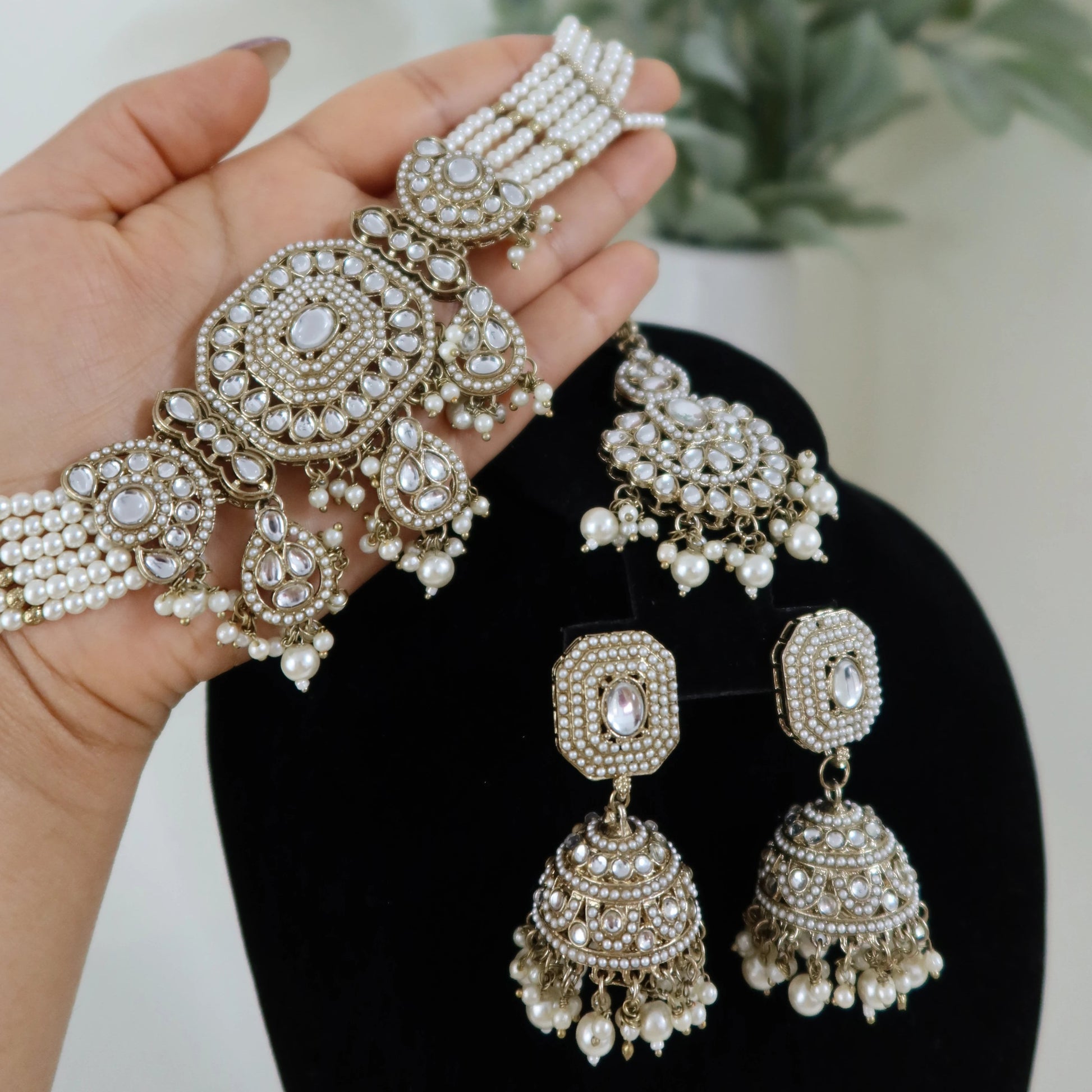 Silver jewelry set including earrings and bangles held by a hand with a blurred plant background