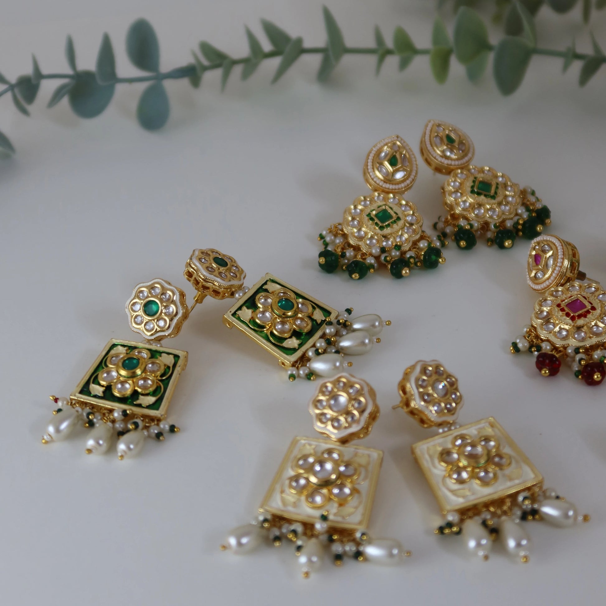 Set of gold and green jewelry pieces on a white surface with green leaves in the background