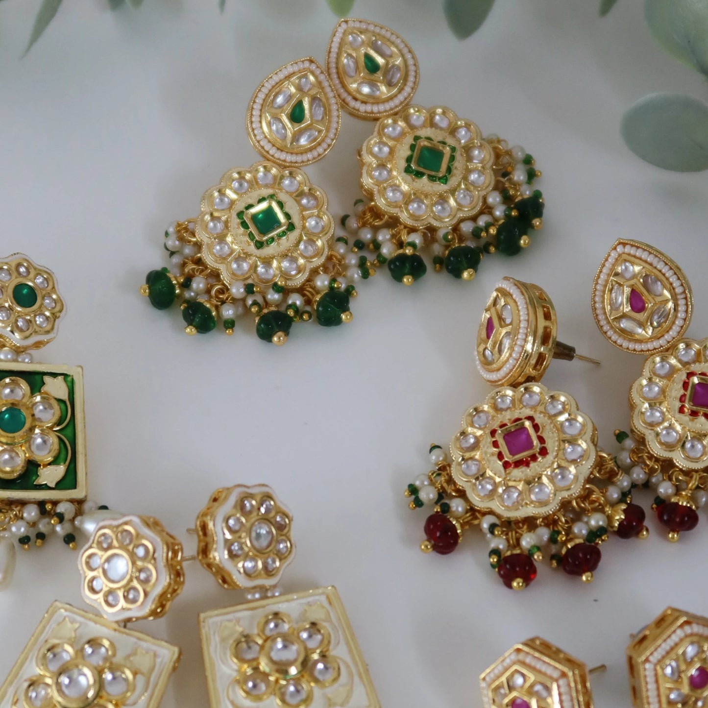 Set of gold earrings with gemstones on a white background with green leaves.