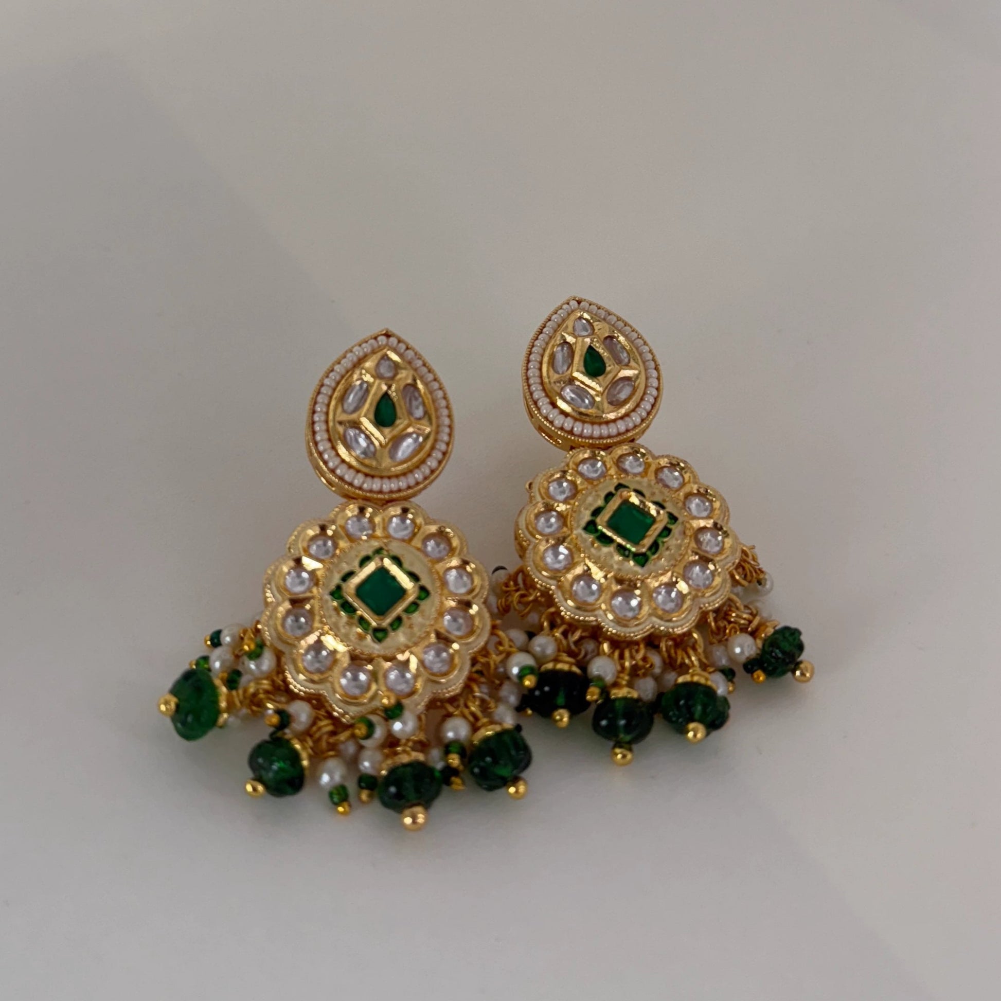 Gold earrings with green and white stones on a light gray background
