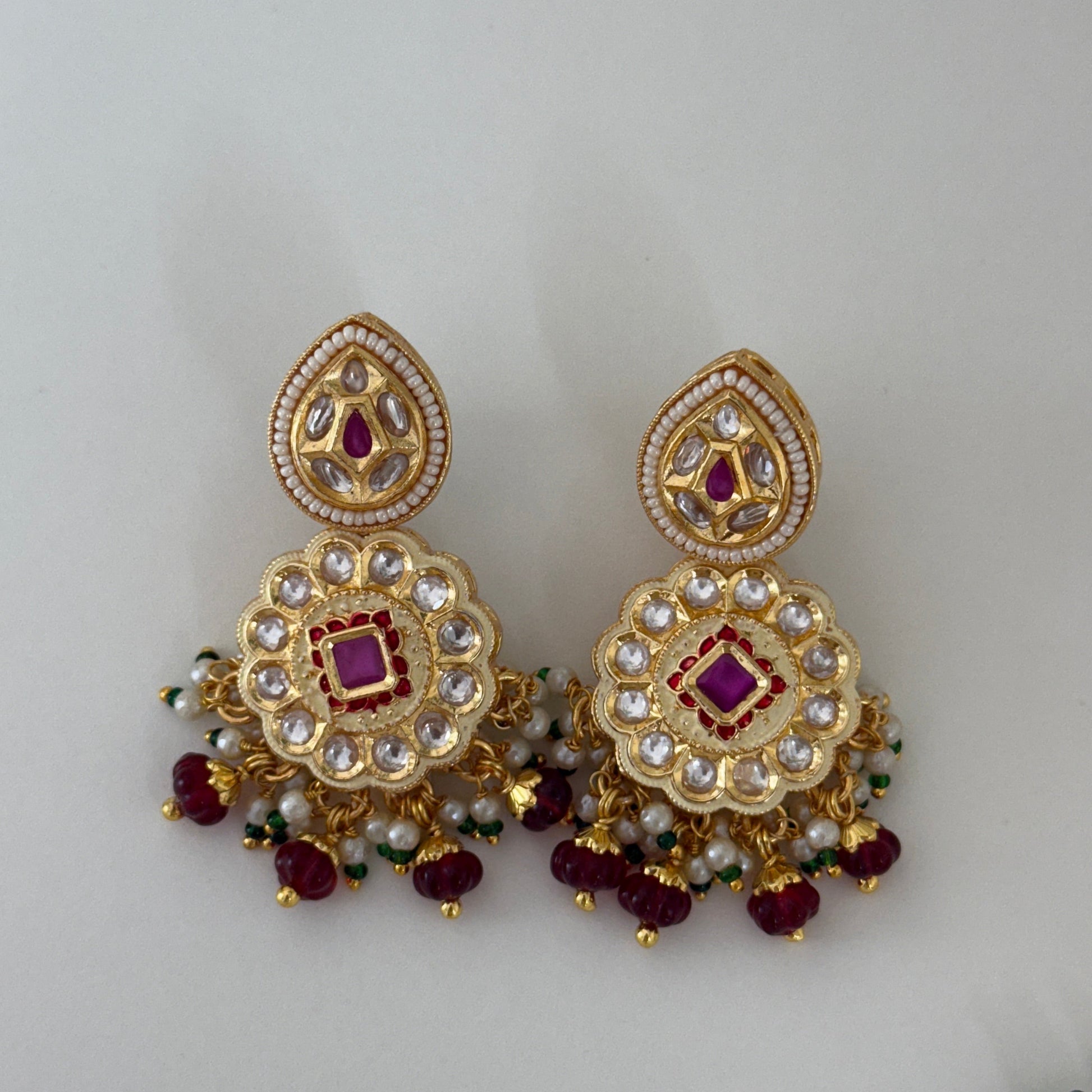 Gold earrings with red and clear stones on a light gray background