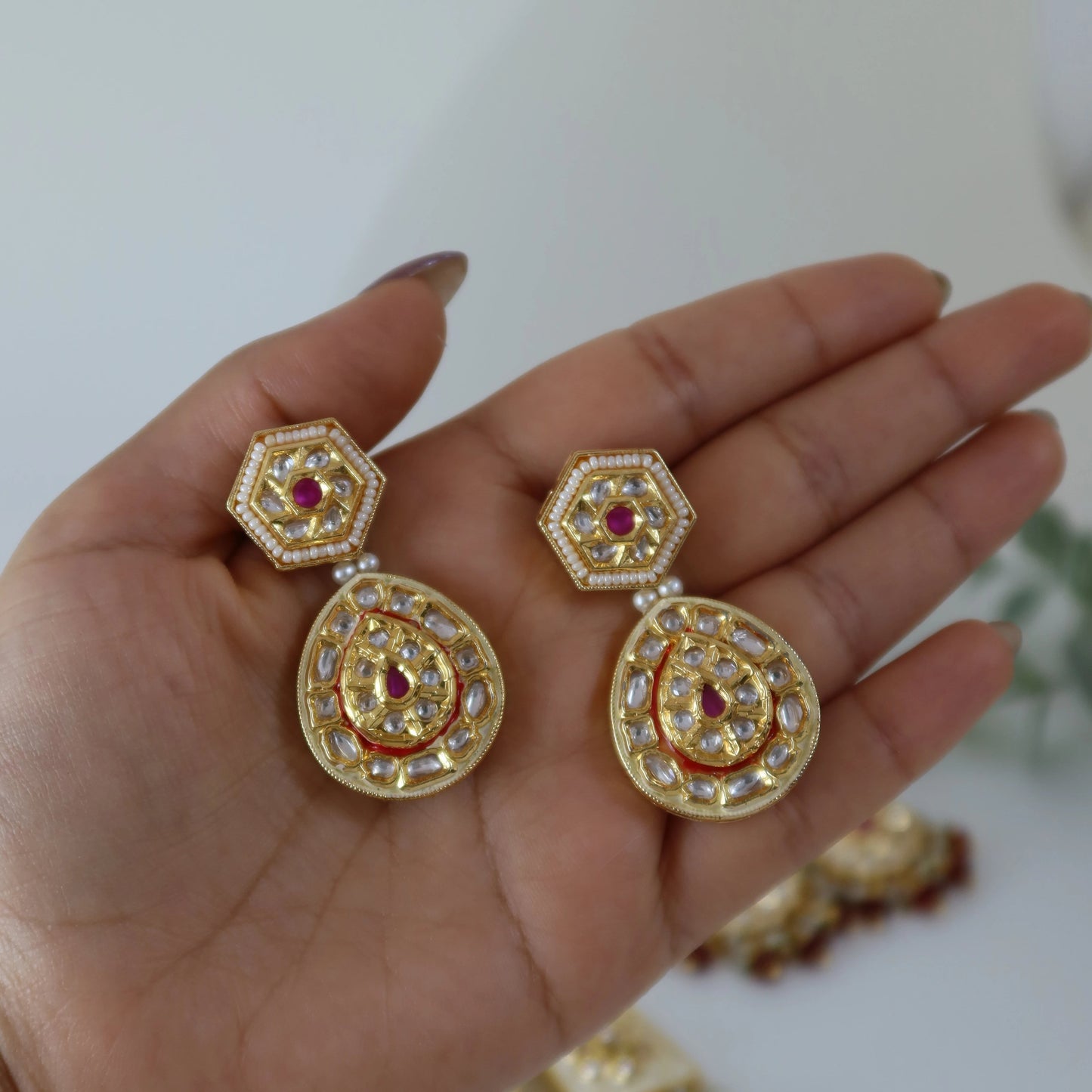 Gold earrings with red gemstones held in a hand against a white background