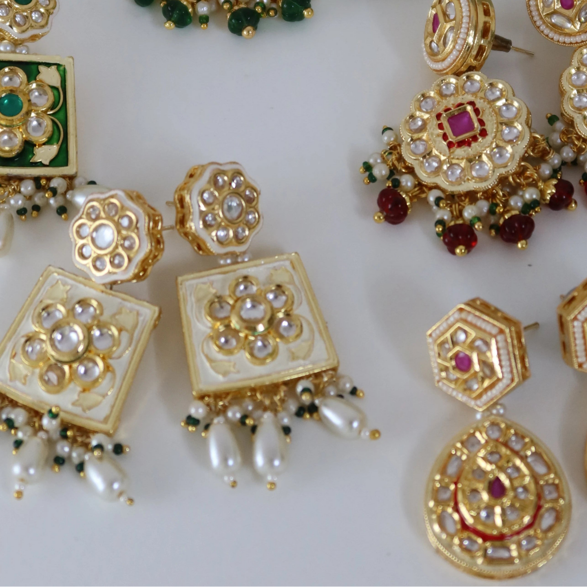 Set of gold earrings with gemstones on a white background with green leaves.