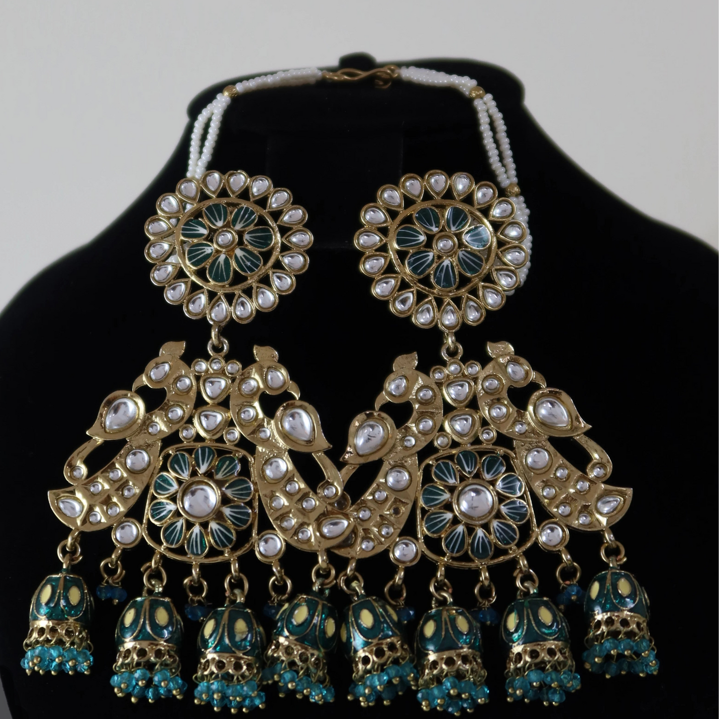 Ornate jewelry set with earrings and necklace on a black stand against a light gray background
