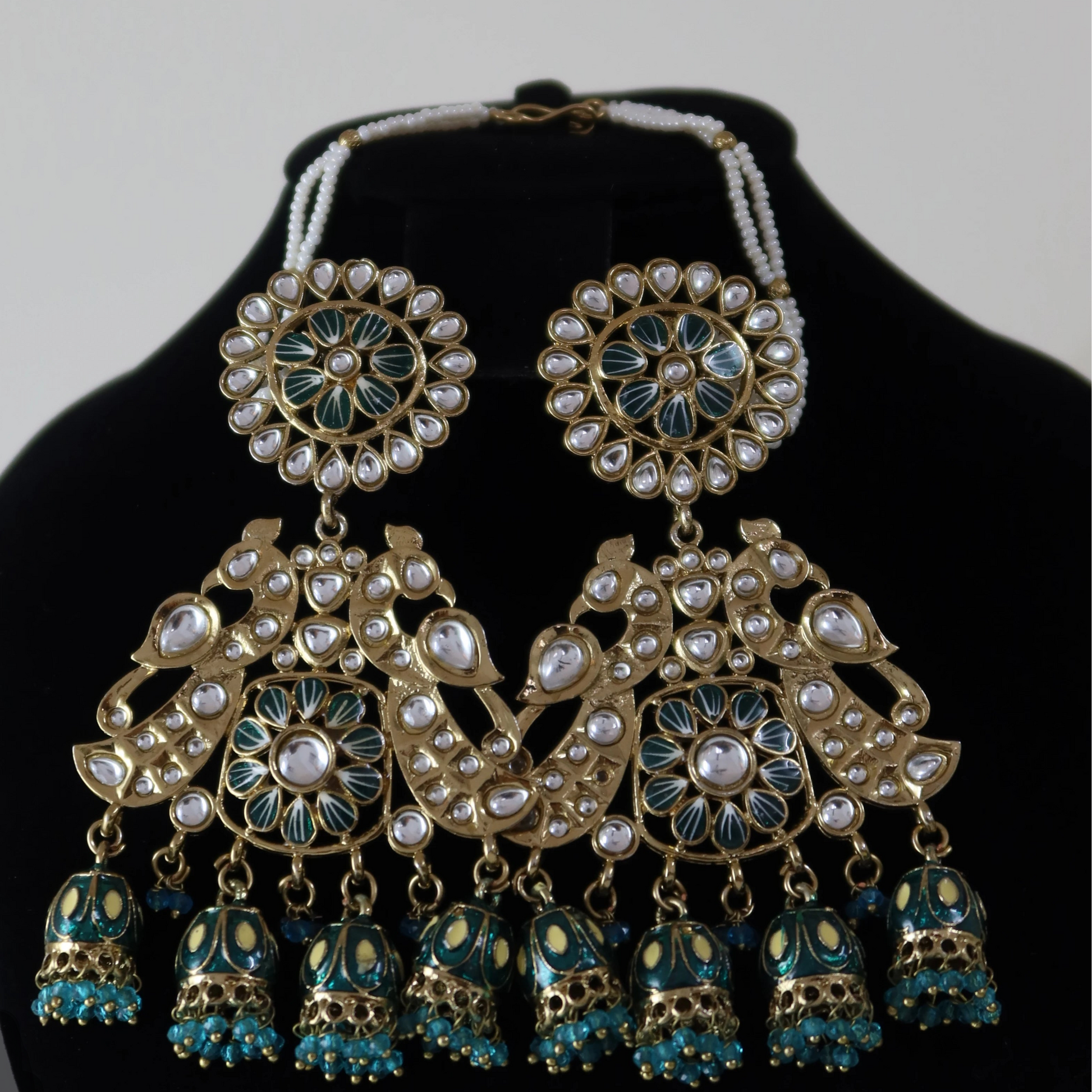Ornate jewelry set with earrings and necklace on a black stand against a light gray background