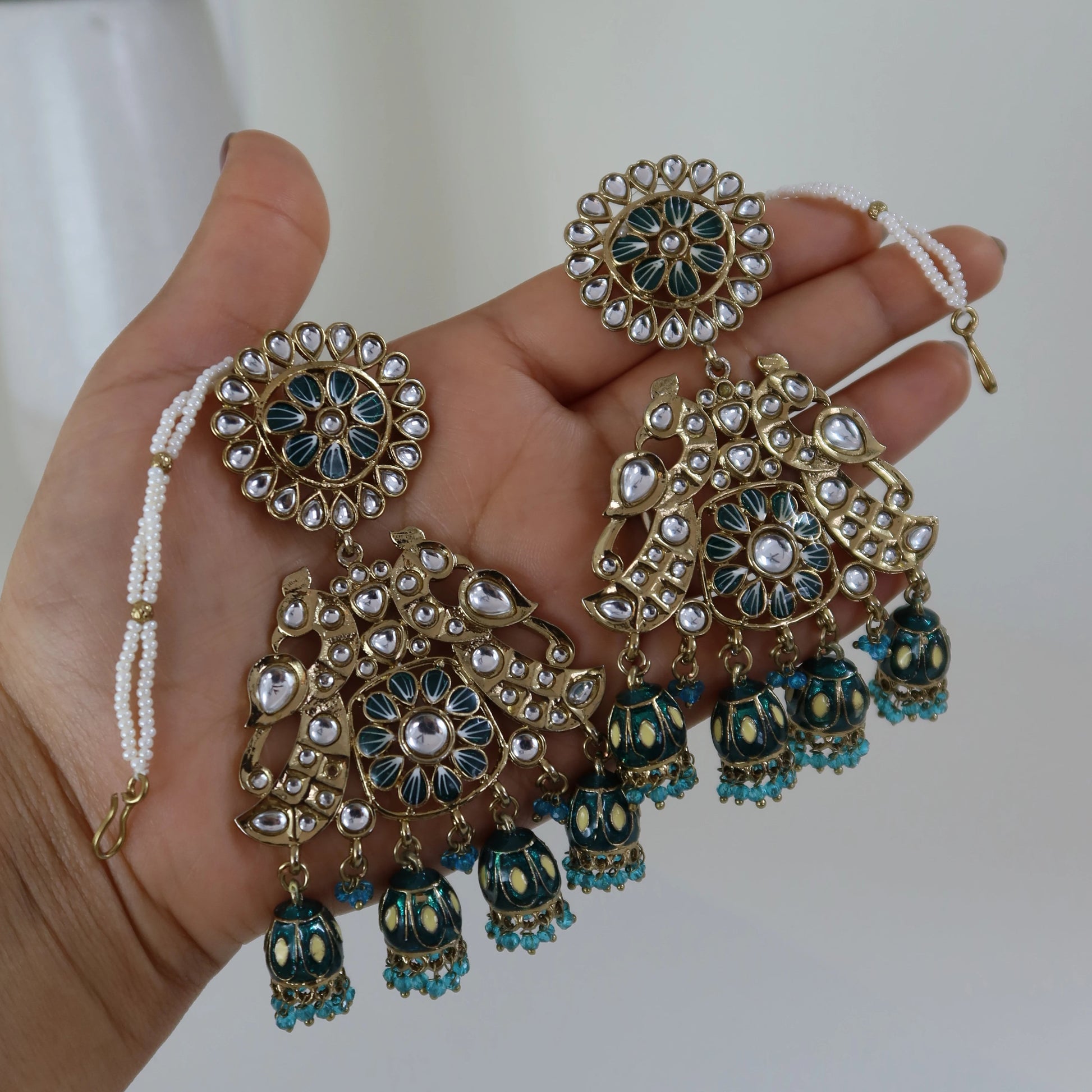 Hand holding decorative jewelry set with green and gold elements against a neutral background