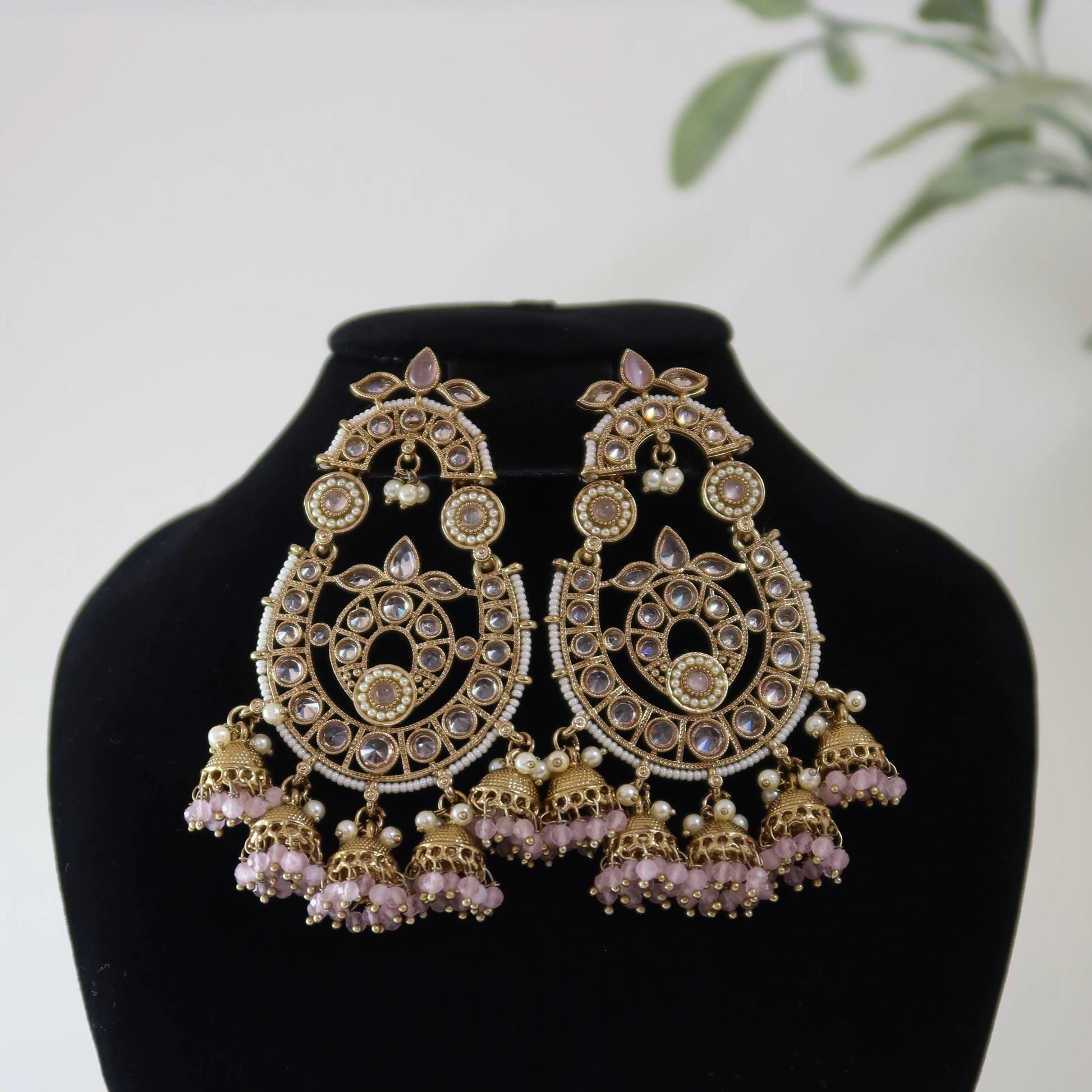 Ornate gold and pink earrings on a black mannequin bust with a white background