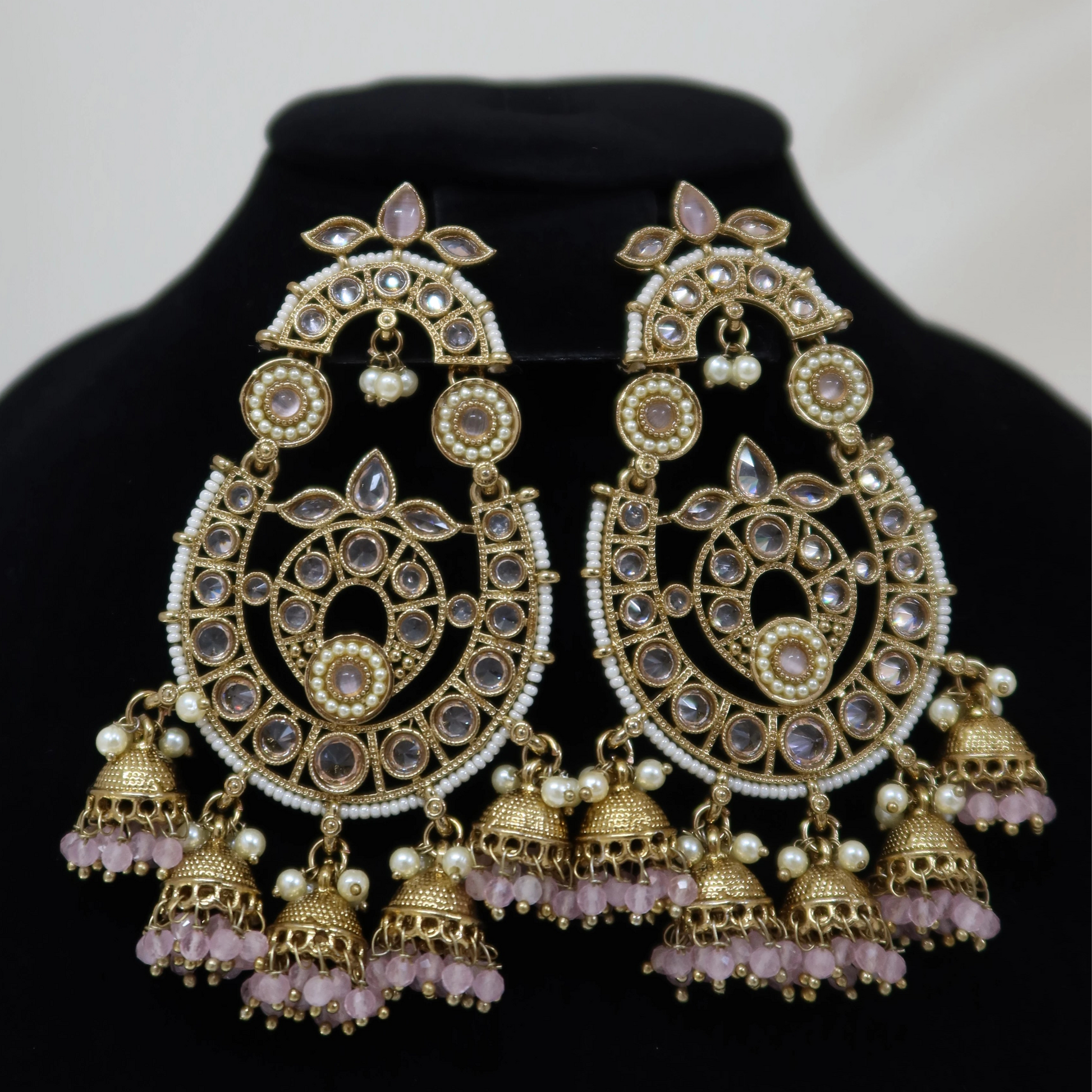 Ornate gold earrings with purple beads on a black stand against a white background
